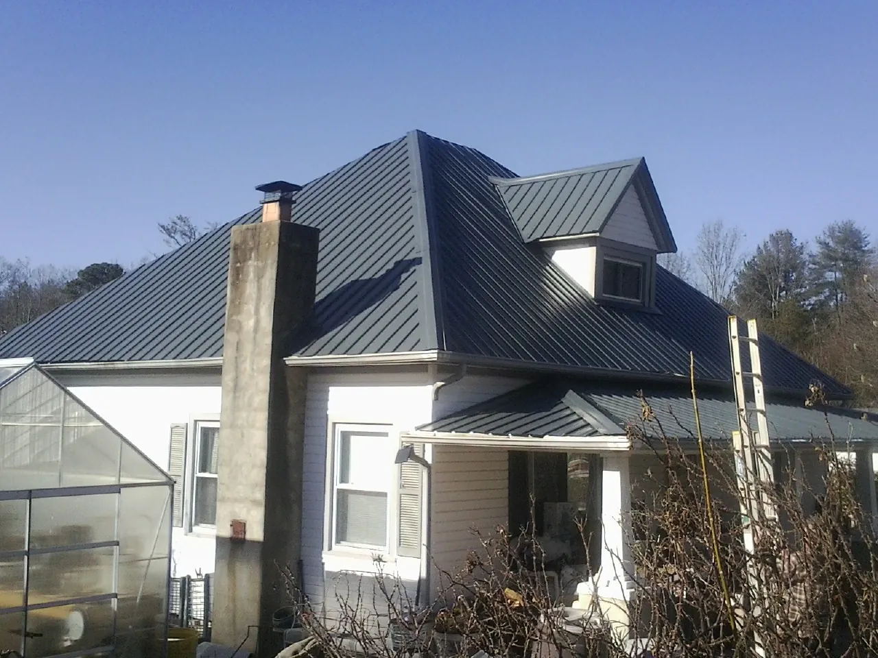 Dark blue standing seam metal roof on a white farmhouse with dormer — Slate & Tile Roof Repair by Roofing Brothers in North Wales