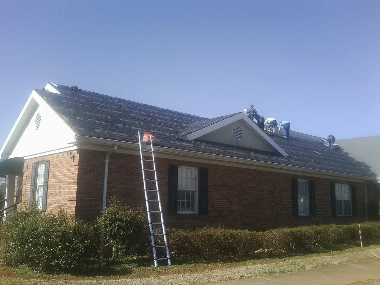 Crew tearing shingles off a brick ranch roof with a ladder set — Emergency Roof Repair work by our crew in North Wales