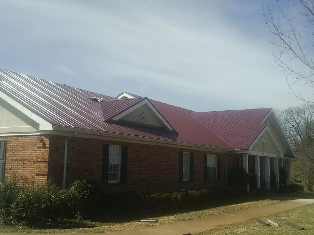 Red metal roof with gabled entries on a long brick building, from a Hail Damage Roof Repair job in North Wales
