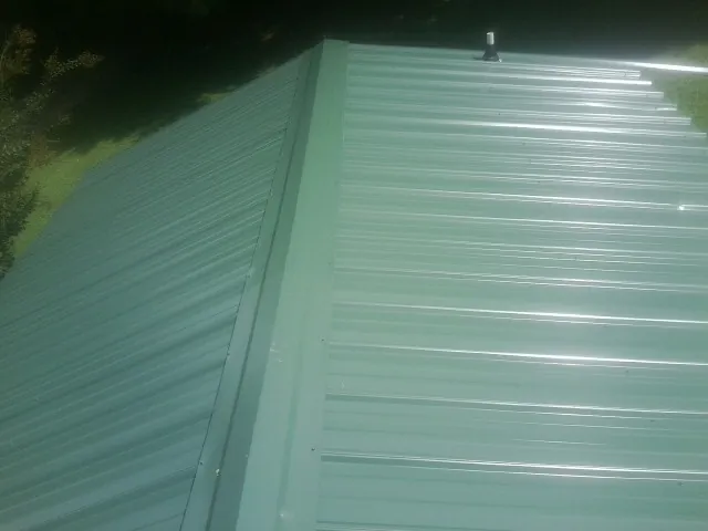 New green metal panels meeting at the ridge of a roof — Flat Roof Repair work by our crew in North Wales