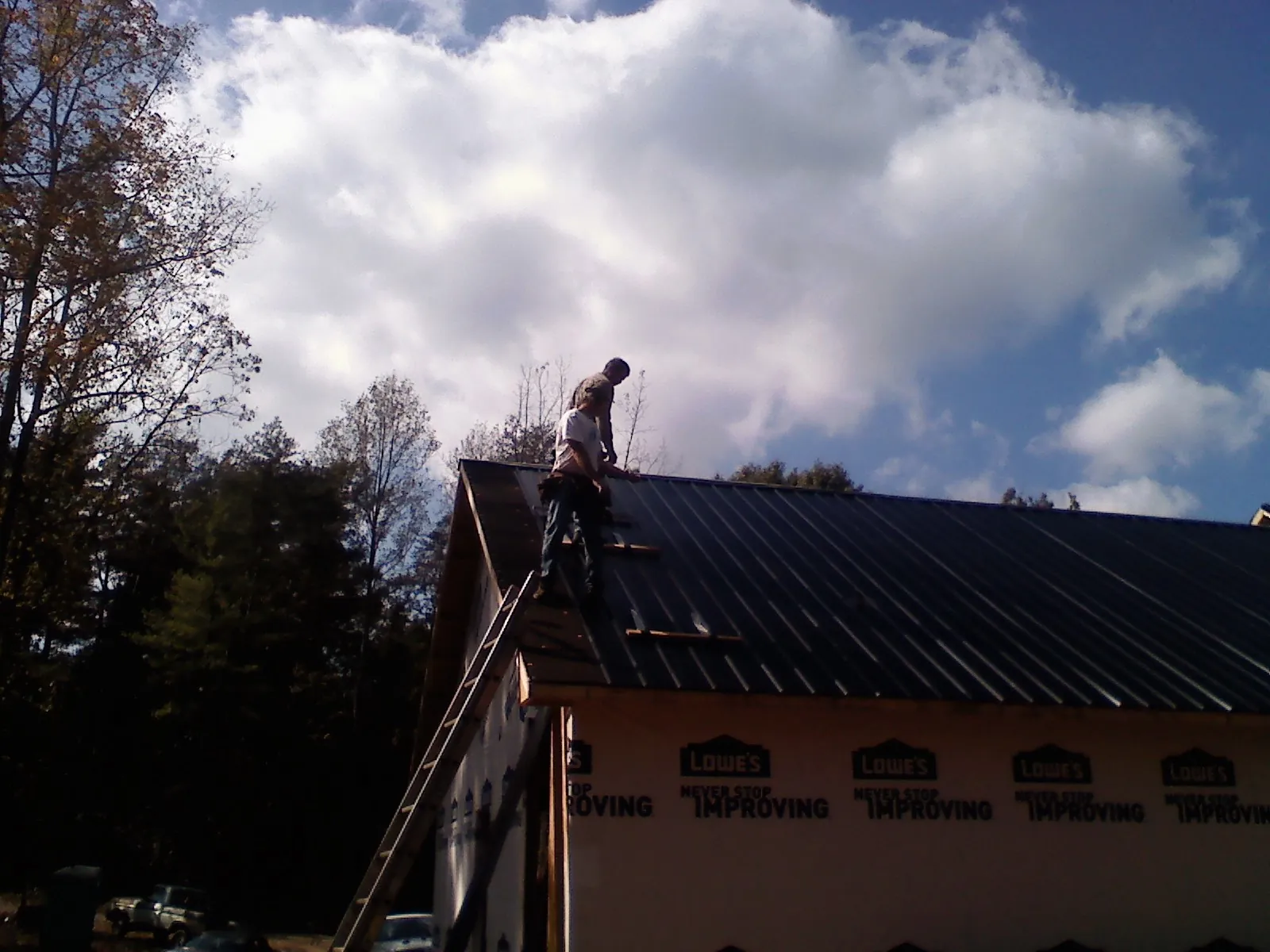 Roofer fastening dark metal panels high against a cloudy sky, from a Roof Inspection job in North Wales