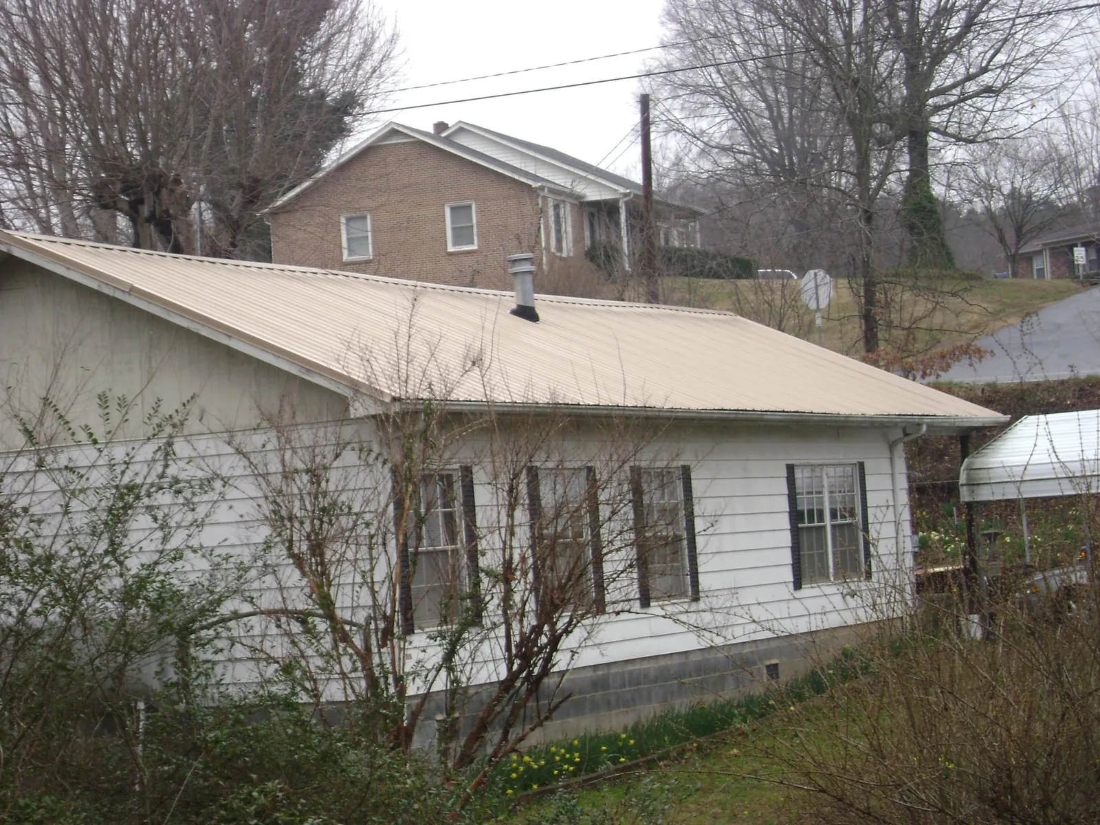 Tan metal roof on a white sided house set into a hillside — Commercial Roofing by Roofing Brothers in North Wales